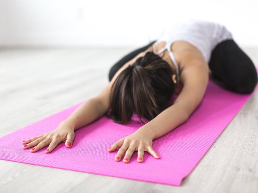 Alumna en Balasana o postura del niño sobre esterilla rosa en estudio de yoga luminoso.